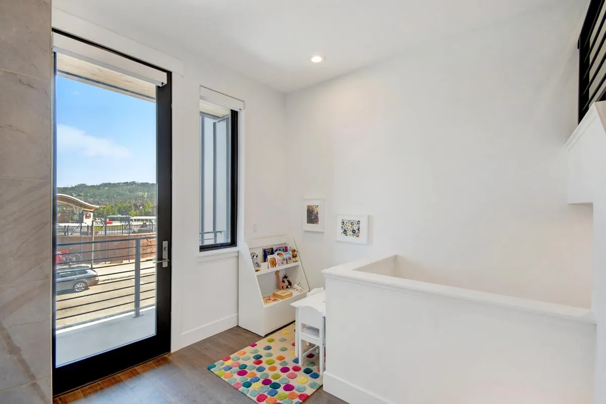 A cheerful children's nook with a small table and chairs set atop a colorful rug, a shelf stocked with toys, and a large window providing ample natural light. The scene is set for reading, art projects, or imaginative play, designed specifically with younger guests in mind.