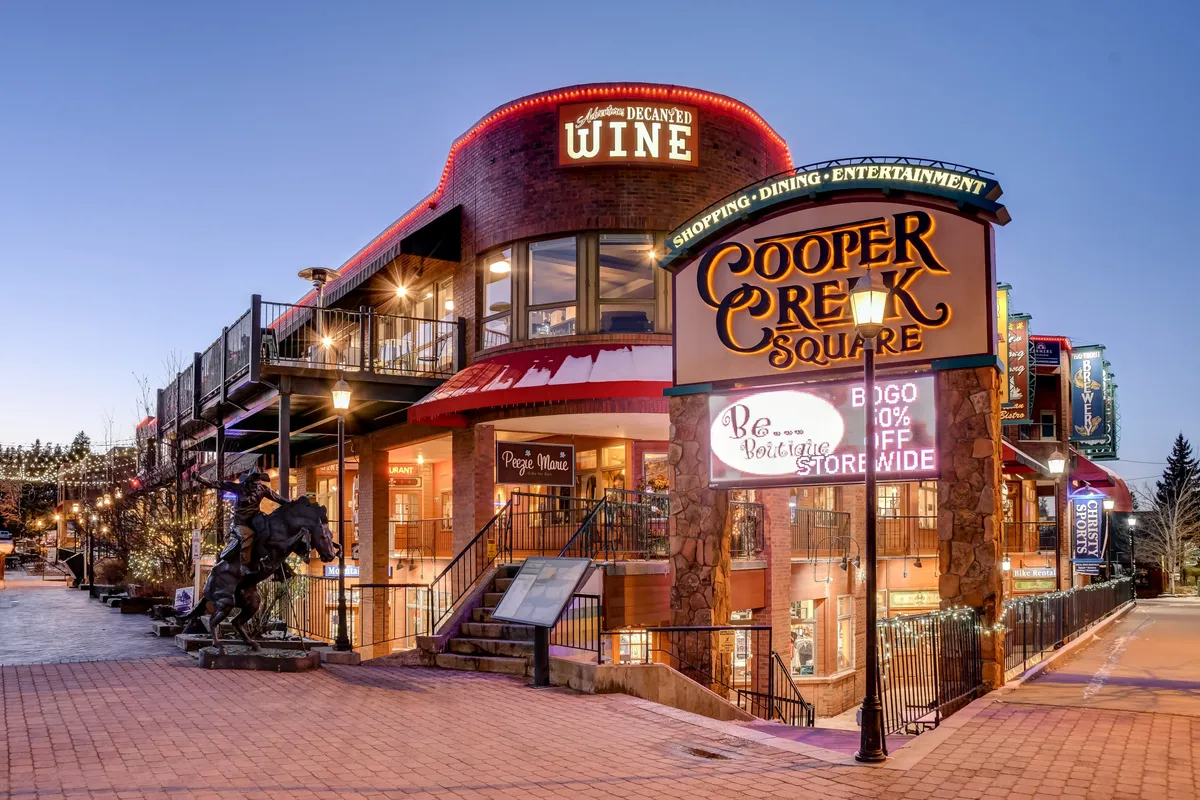 Festive outdoor seating area at Cooper Creek Square, with prominent signage, wine shop, and lively ambiance. The scene features people socializing, shopping, and dining, encapsulating the vibrant local flavor and easy access to restaurants, boutiques, and nightlife described in the narrative.