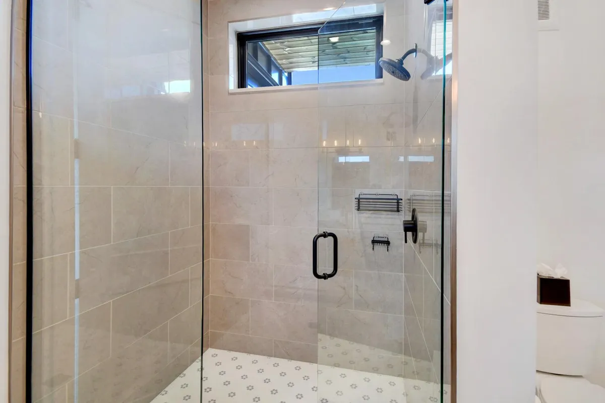 A contemporary bathroom with a glass shower enclosure, modern fixtures, and distinct decorative floor tiles. The design is both refreshing and tranquil, ideal for a rejuvenating shower at any time of day.
