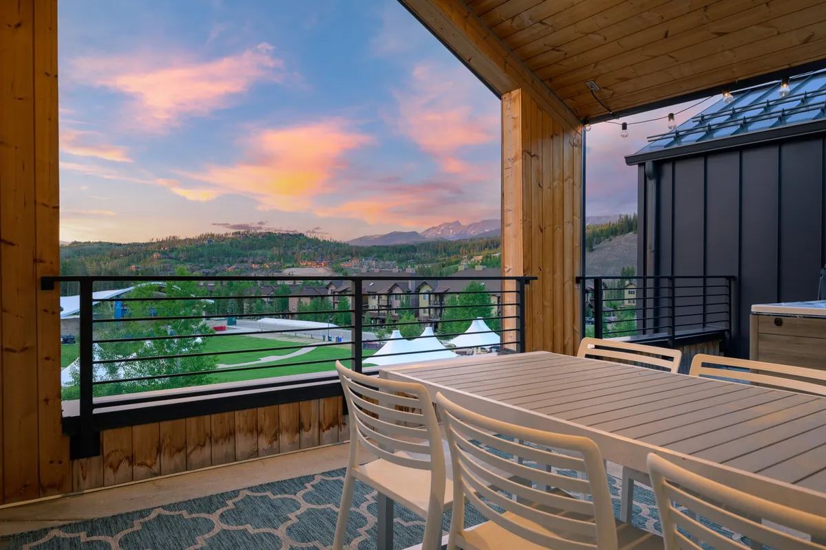 An elegant outdoor dining table set on a rooftop deck, perfectly positioned to capture views of the mountains as the sky glows with the colors of sunset. The scene blends sophistication with the beauty of nature, ideal for memorable meals and celebrations.