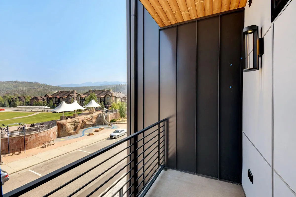 An exterior balcony view overlooking a landscaped area, with striking mountain backdrops and nearby buildings. The vantage point provides a sense of connection between the home and the surrounding recreational spaces, ideal for both relaxation and watching park activities.