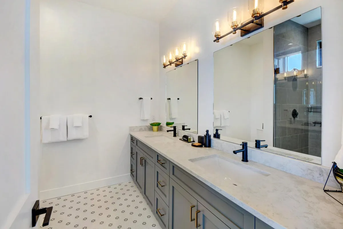 A modern, spa-inspired bathroom with a double vanity, expansive mirrors, and elegant light fixtures. The clean design and inviting atmosphere evoke a sense of calm, perfect for self-care routines and relaxation.